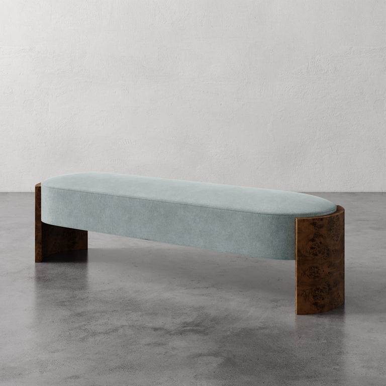 Lemieux et Cie Benoit Custom Upholstered Bench in pale blue with curved Maple burl legs, shown on polished concrete floor against textured plaster walls.