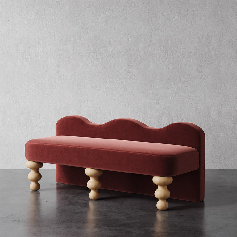 Lemieux et Cie Celine Custom Upholstered Bench in terracotta velvet with scalloped back and hand-turned wood legs, shown on dark wood floor against textured white wall.