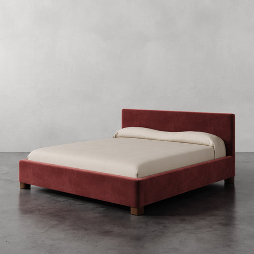 Lemieux et Cie Gérard Bed, low-profile platform bed with wrapped headboard and rounded block feet, shown on polished concrete floor against neutral plaster walls.