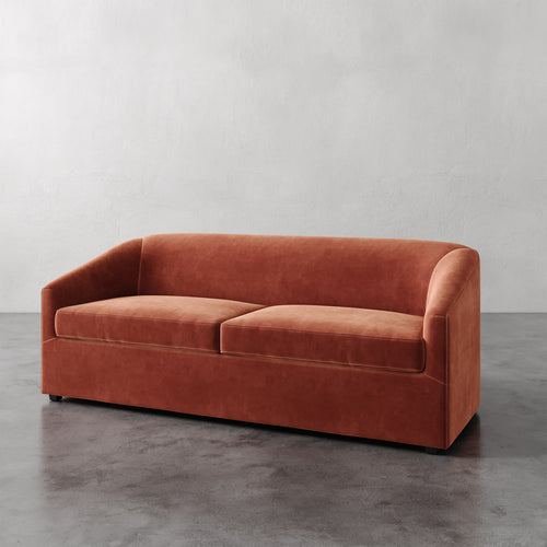 Lemieux et Cie Arvelle Queen Sleeper sofa in warm terracotta, curved arms and low-profile form, shown on polished concrete floor against neutral plaster walls.