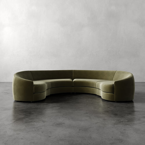 Lemieux Et Cie Rulmann 4-Piece Sectional Curved green sofa on a gray concrete floor with a plain gray wall background