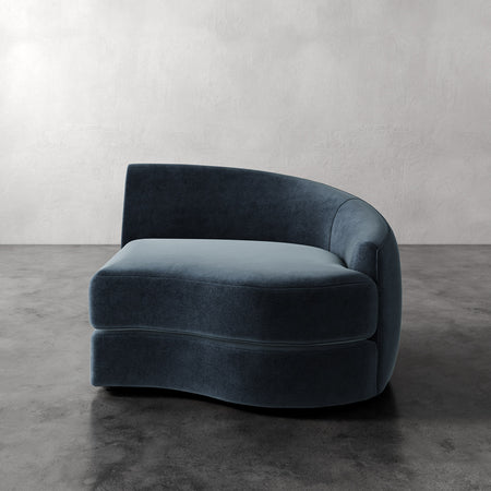 Lemieux et Cie Rulmann Right Arm Chair in deep teal upholstery, curved lounge chair on concrete floor against white plaster wall.