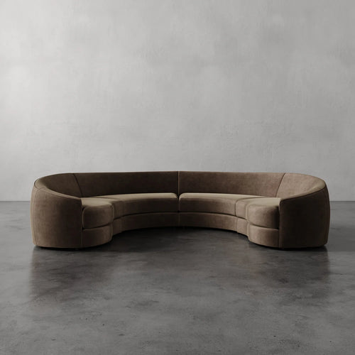 Lemieux Et Cie Rulmann 4-Piece Sectional Brown curved sofa on a gray floor with a plain gray wall background