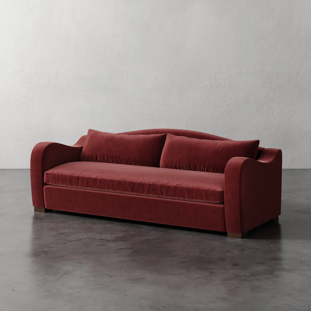Lemieux et Cie Elodie Sofa in deep rust upholstery, bench seat sofa with rounded arms, shown on polished concrete floor against neutral plaster walls.