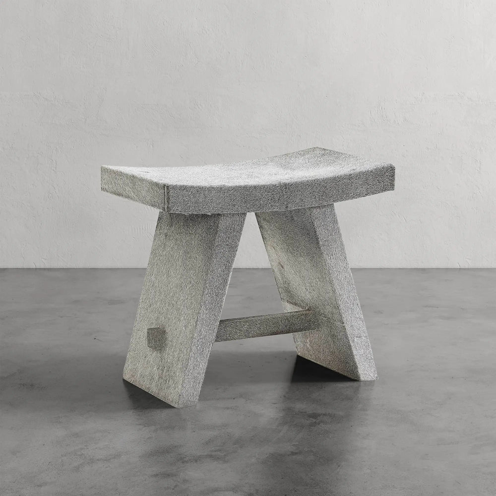 Lemieux et Cie Pierre Stool with curved saddle seat and angled legs, sculptural stool shown on polished concrete floor against neutral plaster walls.