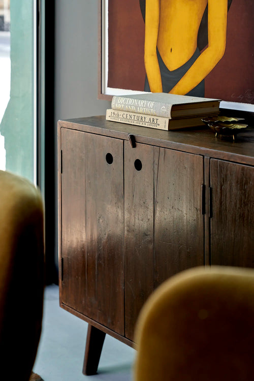 Lemieux et Cie Pierre Jeanneret four-door teak cabinet, angled view with recessed circular pulls, styled with art books and a brass dish