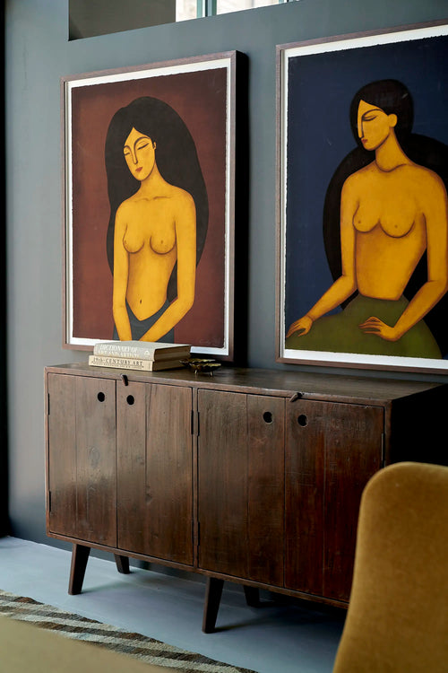 Lemieux et Cie Pierre Jeanneret teak cabinet, three-quarter view showing the tapered legs and recessed circular pulls, styled with framed art and a velvet armchair