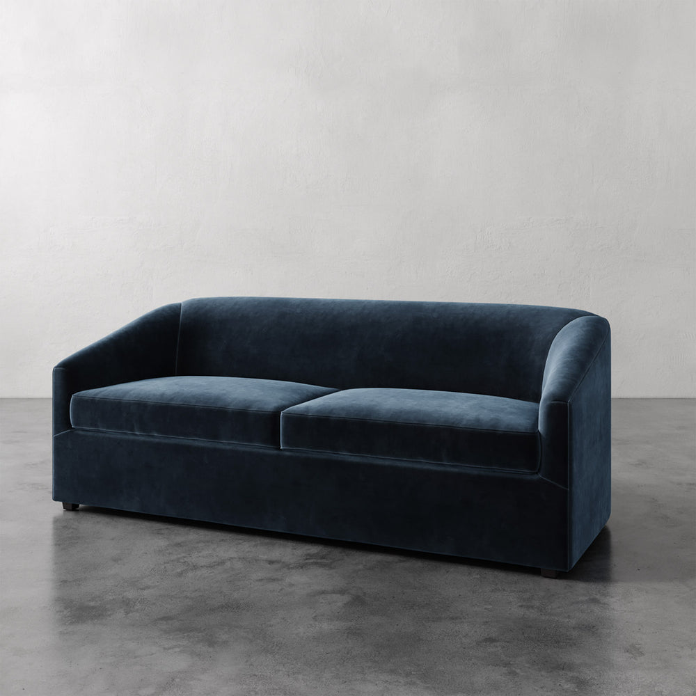 Lemieux et Cie Arvelle Queen Sleeper in deep navy, two-cushion sofa with rounded arms, shown on polished concrete floor against white walls.