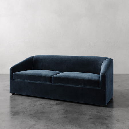 Lemieux et Cie Arvelle Queen Sleeper in deep navy, two-cushion sofa with rounded arms, shown on polished concrete floor against white walls.