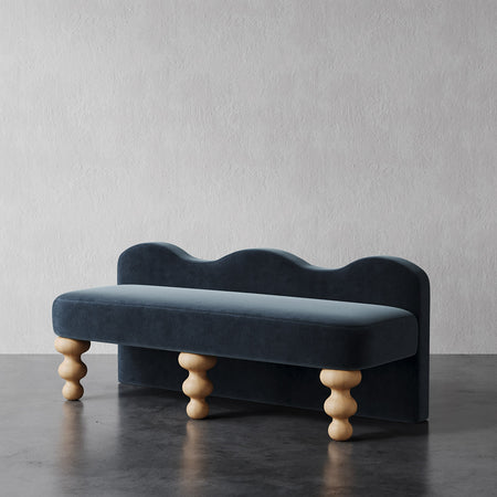 Lemieux et Cie Celine Custom Upholstered Bench in deep blue velvet with hand-turned wood legs, shown on dark concrete floor against textured plaster wall.