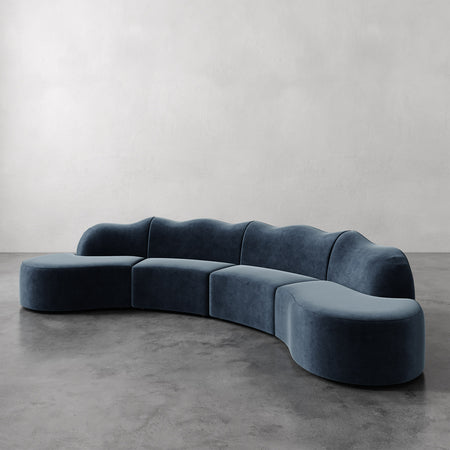 Lemieux et Cie Serpentine Sectional Sofa in blue-gray velvet, sculptural modular sofa with rounded organic forms on polished concrete floor.