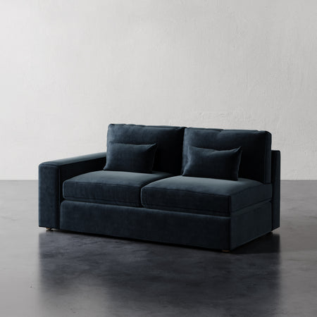 Lemieux et Cie Lacroix Left or Right Arm Loveseat in deep charcoal upholstery, modular sofa with rectilinear form, on dark concrete floor against textured plaster walls.