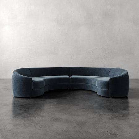 Lemieux et Cie Rulmann 4-Piece Sectional in charcoal blue, curved modular sofa on polished concrete floor against textured plaster wall.