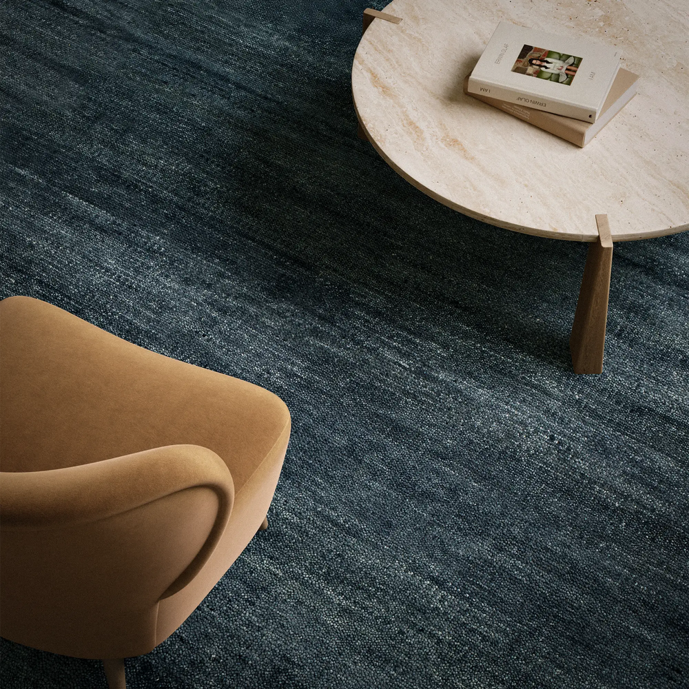 Lemieux et Cie Rochefort Rug in indigo, hand-knotted New Zealand wool and cotton, shown with sculptural side table and upholstered chair in warm neutral sitting room.