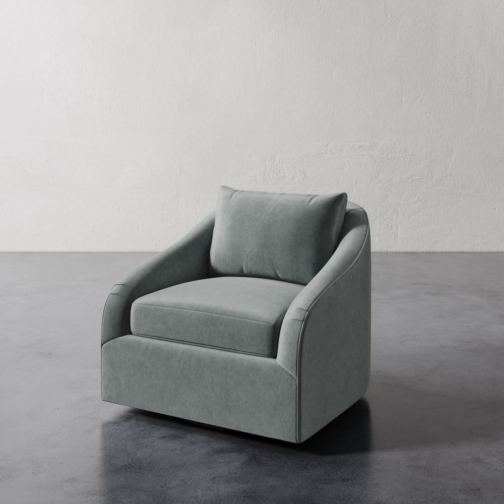 Lemieux et Cie Rousseau Swivel Chair in sage upholstery, sculptural lounge chair with sloped arms on dark concrete floor against plaster walls.