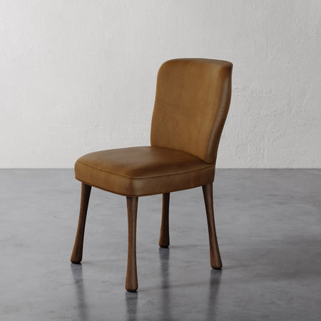 Lemieux et Cie Rozette Dining Chair in tobacco leather with tapered legs, side chair shown on polished concrete floor against textured white walls.