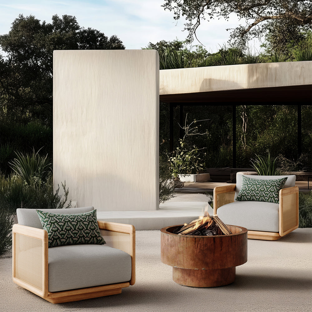 Lemieux et Cie Dock Teak Lounge Chair with woven cane panels and solid teak frame, outdoor seating on stone patio with fire bowl and modern architecture.