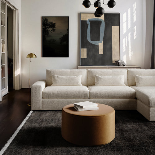 Lemieux et Cie Sophie Round Ottoman in ivory bouclé, low-profile seating styled with sectional sofa in sitting room with white walls and dark wood floors.