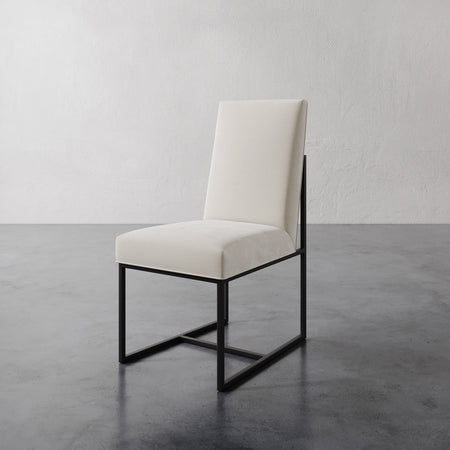 Lemieux et Cie Dupont Dining Side Chair with upholstered ivory seat and back on dark metal frame, shown on polished concrete floor against textured plaster walls.