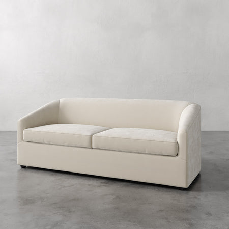 Lemieux et Cie Arvelle Queen Sleeper in ivory, low-profile sofa with rounded arms, shown on polished concrete floor against neutral plaster wall.