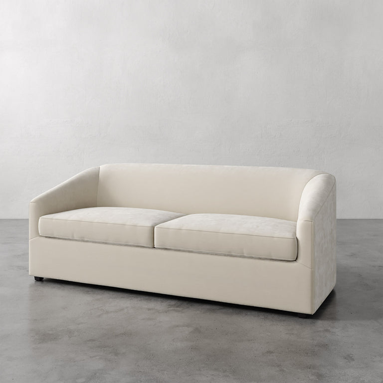 Lemieux et Cie Arvelle Queen Sleeper in ivory, low-profile sofa with rounded arms, shown on polished concrete floor against neutral plaster wall.