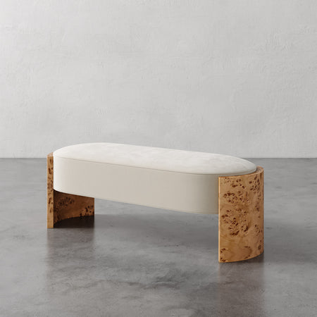Lemieux et Cie Benoit Bench with curved Maple burl legs and ivory upholstered seat, low-profile bench on polished concrete floor against textured plaster wall.