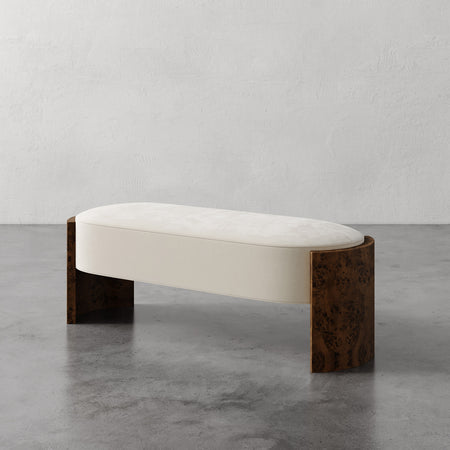 Lemieux et Cie Benoit Custom Upholstered Bench in ivory with curved Maple burl legs, low-profile seating on concrete floor against plaster walls.