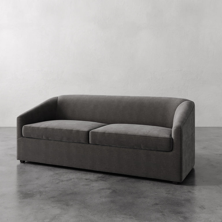 Lemieux et Cie Lemieux et Cia Arvelle Queen Sleeper in charcoal, sofa with curved arms and low profile, shown on concrete floor against neutral wall.