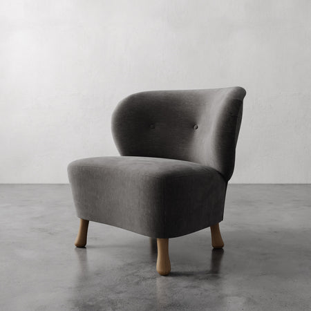 Lemieux et Cie Tourenne Chair with sculptural turned wood legs, low-profile slipper chair on concrete floor against neutral plaster walls.