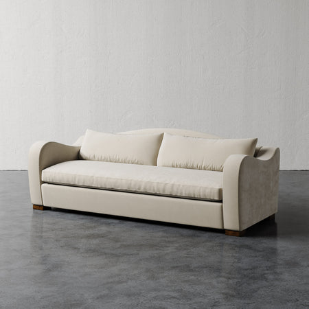 Lemieux et Cie Elodie Sofa with bench seat in neutral upholstery, sculptural rounded arms, shown on polished concrete floor against textured plaster walls.