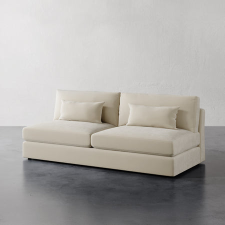 Lemieux et Cie Lacroix Armless Sofa in ivory upholstery, modular sofa with bolster pillows, shown on polished concrete floor against white walls.