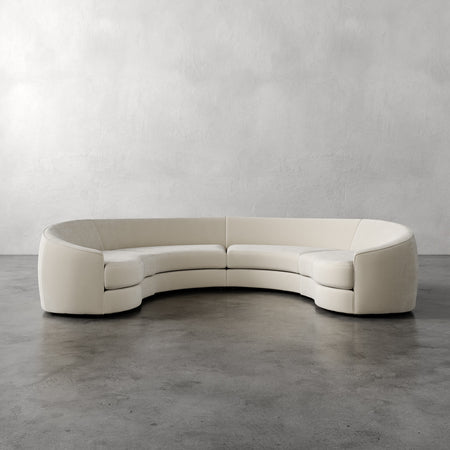 Lemieux et Cie Rulmann 4-Piece Sectional in ivory, curved modular sofa with rounded arms, shown on polished concrete floor against textured plaster walls.