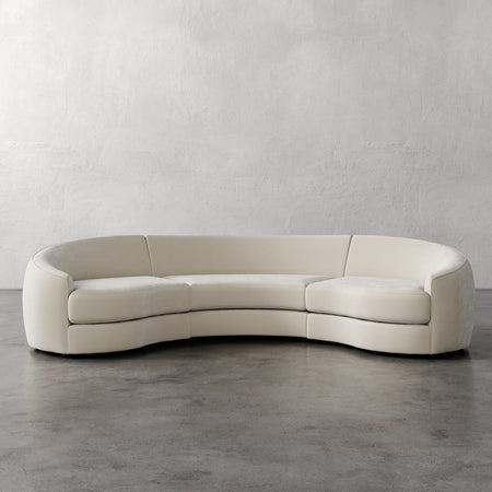 Lemieux et Cie Rulmann 3-Piece Sectional in ivory, curved low-profile sofa on concrete floor against textured plaster walls.