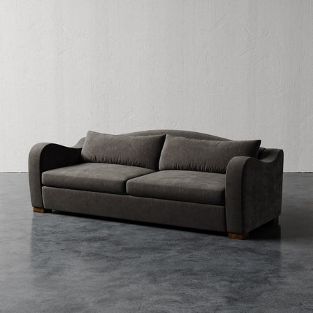 Lemieux et Cie Elodie Sofa in charcoal upholstery, low-profile sofa with rounded arms, shown on polished concrete floor against textured plaster walls.