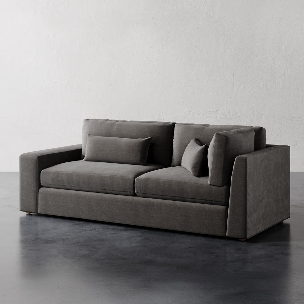 Lemieux et Cie Lacroix Sofa in charcoal upholstery, modular sofa with deep cushions and bolster pillows, on dark wood floors against white plaster walls.