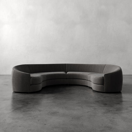 Lemieux et Cie Rulmann 4-Piece Sectional in charcoal, curved modular sofa on concrete floor against textured plaster walls.