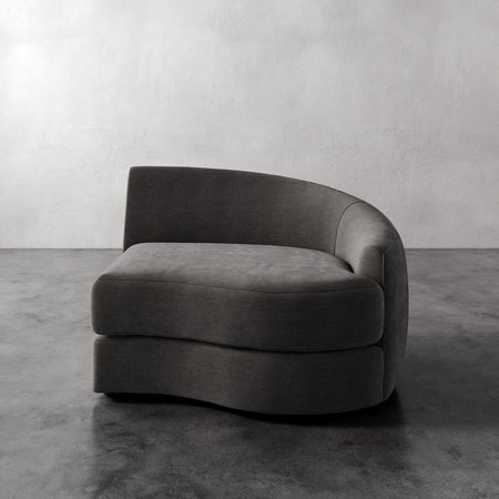 Lemieux et Cie Rulmann Right Arm Chair in charcoal upholstery, curved lounge chair with sculptural form, shown on concrete floor against plaster walls.