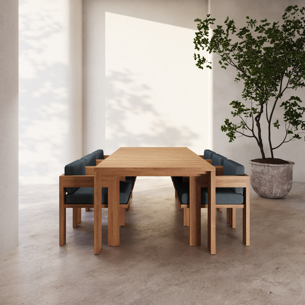 Lemieux et Cie S2 Teak 84" Rectangular Dining Table in solid teak wood with upholstered chairs, stone floor in warm light with white walls.