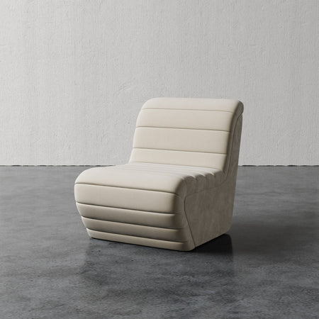 Lemieux et Cie Brunoy Chair, channel-quilted slipper chair in ivory upholstery, shown on concrete floor against textured plaster walls.