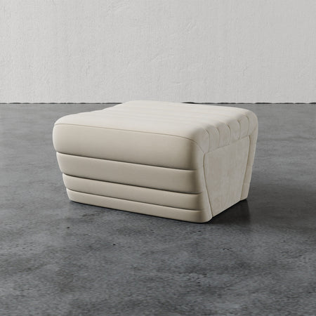 Lemieux et Cie Brunoy Ottoman in ivory with horizontal channel tufting, upholstered ottoman on polished concrete floor against textured plaster walls.