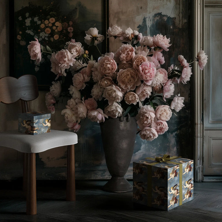 Lemieux et Cie Cupid’s Bow fancy gift wrapping with cherubs inspired by Renaissance art, in a dark room with pink flowers in the Louis vase next to the Madeleine dining chair