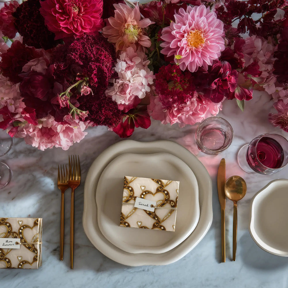 Lemieux et Cies Valentines Day tablescape featuring the Bijou Amour white and gold wrapping paper on a marble table with the Amorphous dinnerware and lush red and pink flowers