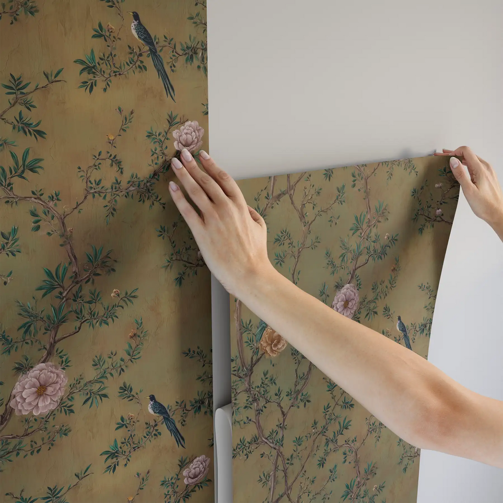 Lemieux et Cie Vertivier Wallpaper in warm gold with birds and blush peonies, chinoiserie pattern shown being installed on neutral walls.