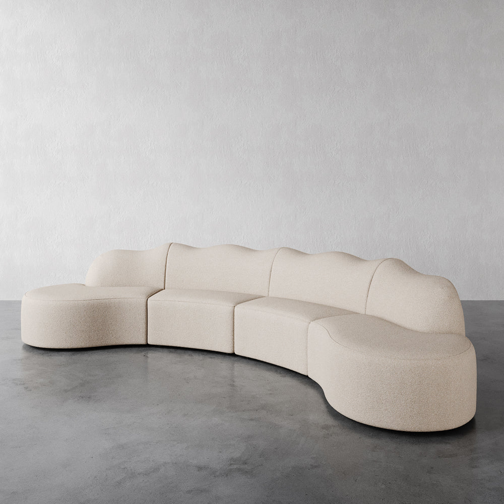 Lemieux et Cie Serpentine 4 Piece in Vista Vanilla bouclé, modular sectional sofa with sculptural rounded forms, shown on concrete flooring against white walls.