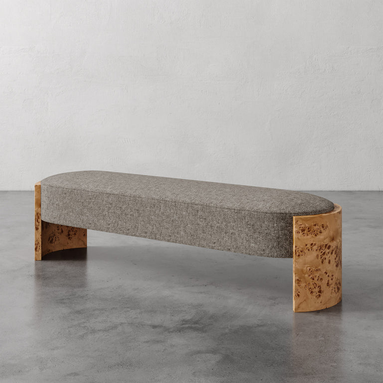 Lemieux et Cie Benoit Custom Upholstered Bench in grey upholstery with curved Maple burl legs, shown on polished concrete floor against white wall.