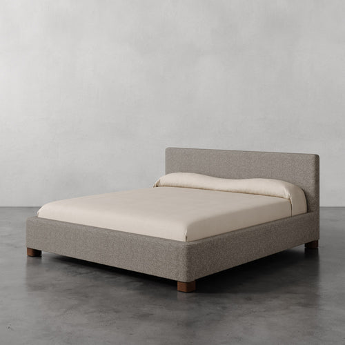 Lemieux et Cie Gérard Bed, low-profile platform bed with wrapped headboard and rounded block feet, shown on polished concrete floor against neutral walls.