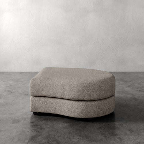 Lemieux Et Cie Rulmann Right Ottoman Beige ottoman on a gray concrete floor with a white wall background