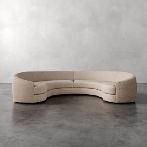 Lemieux Et Cie Rulmann 4-Piece Sectional Beige curved sofa on a gray floor with a plain gray wall background