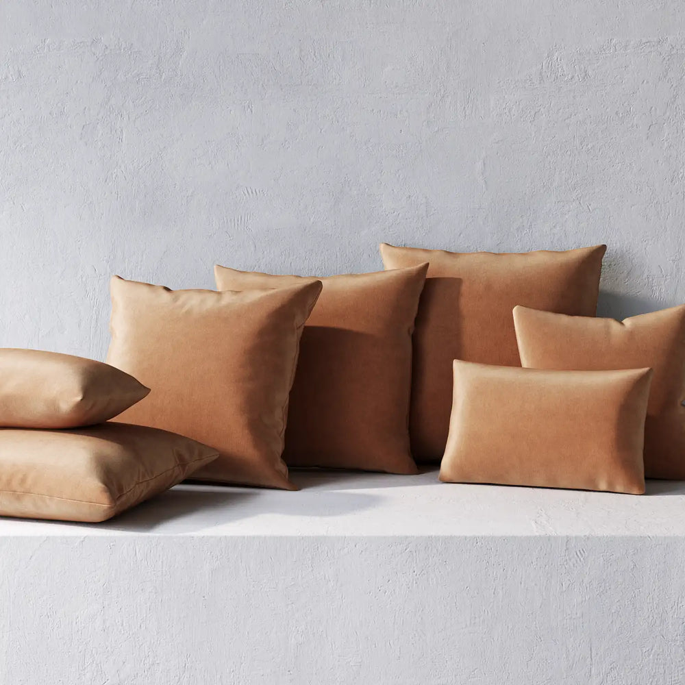 Lemieux et Cie Throw Pillows in warm terracotta tones, non-welted rectangular and square cushions arranged on textured plaster shelf against white wall.