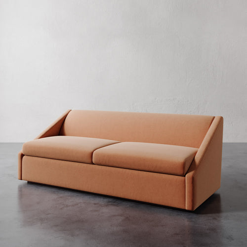 Lemieux et Cie Fontaine Sofa in warm terracotta upholstery, sofa with architectural silhouette shown on concrete floor against textured plaster walls.
